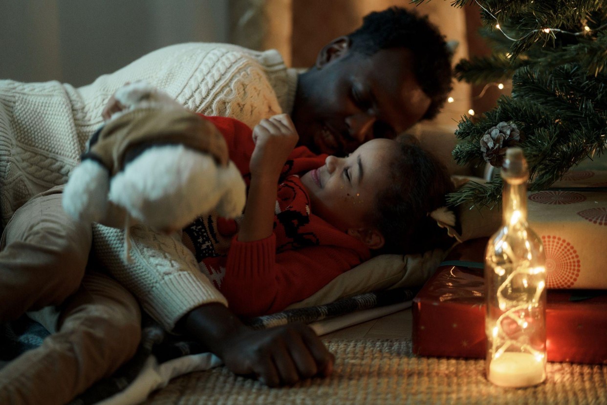 Father and daughter are lying on the floor beside Christmas tree
